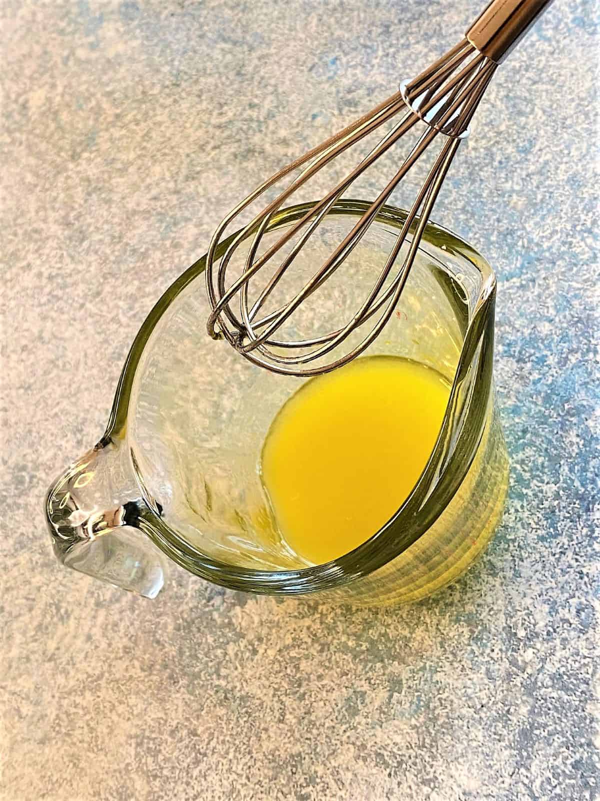 Clear glass measuring cup with small amount of yellow marinade and whisk