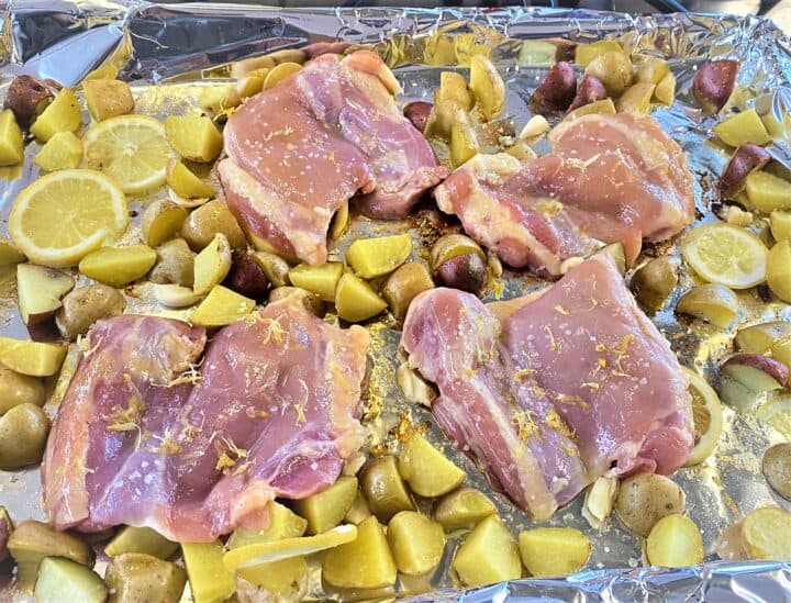 Raw chicken thighs on sheet pan with potato chunks and lemon