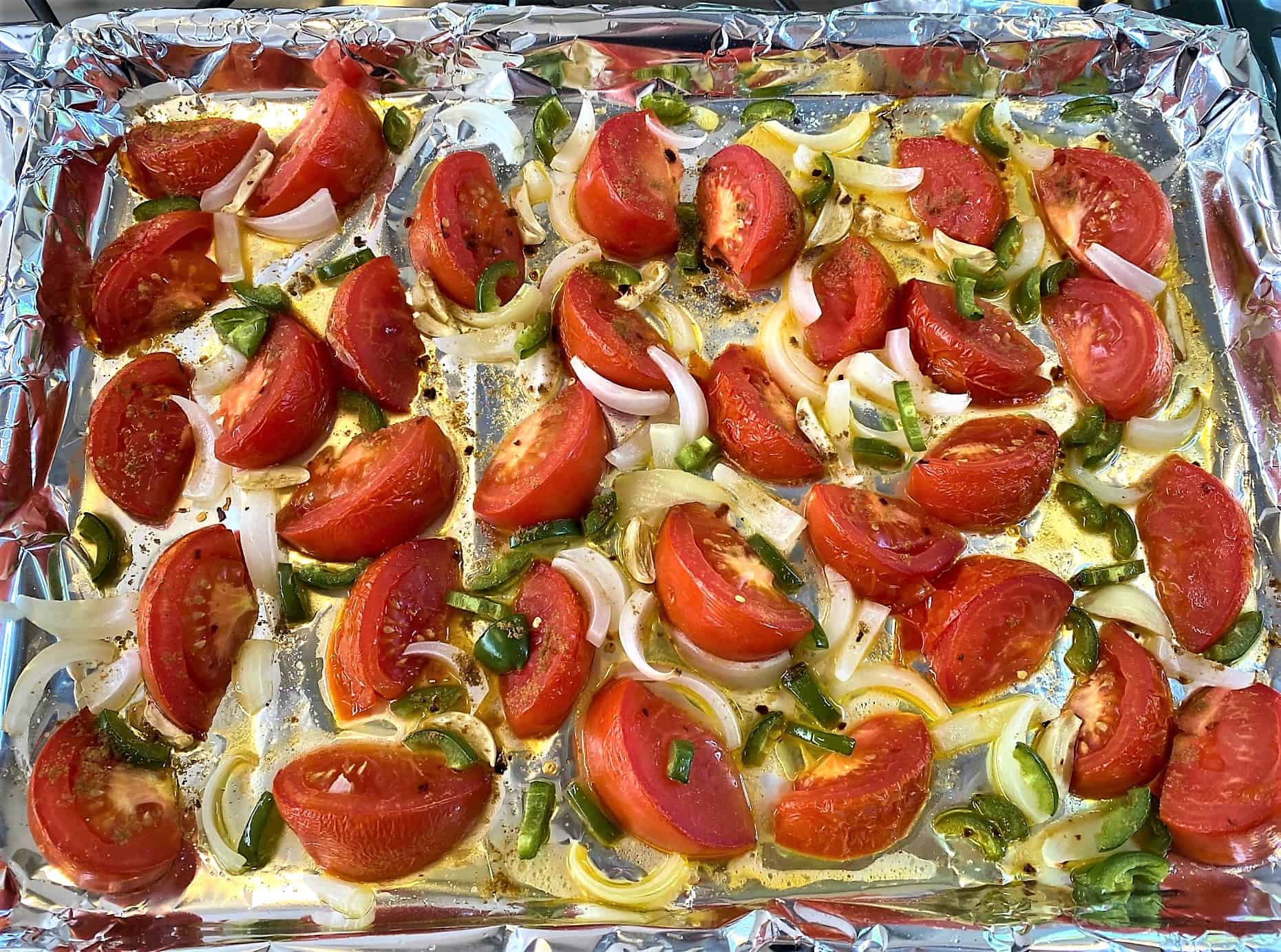 Barely cooked tomato wedges, green peppers, onions and seasonings on foil-lined sheet pan