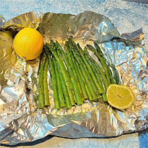 Grilled asparagus on foil with a whole lemon and half lemon and seasonings