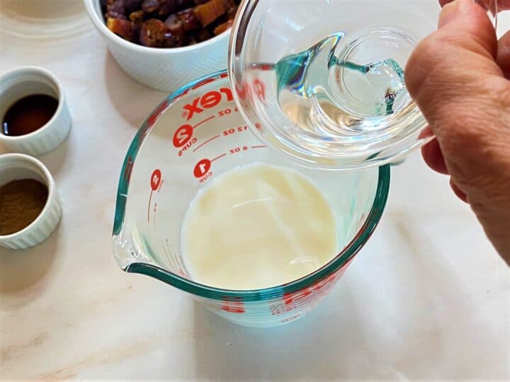 Adding clear white vinegar to milk in a measuring cup, close up