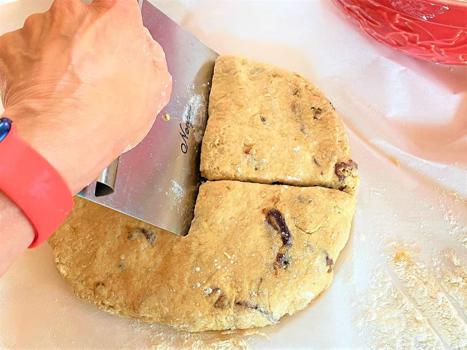 Hand cutting a dough round with a dough scraper on white parchment paper