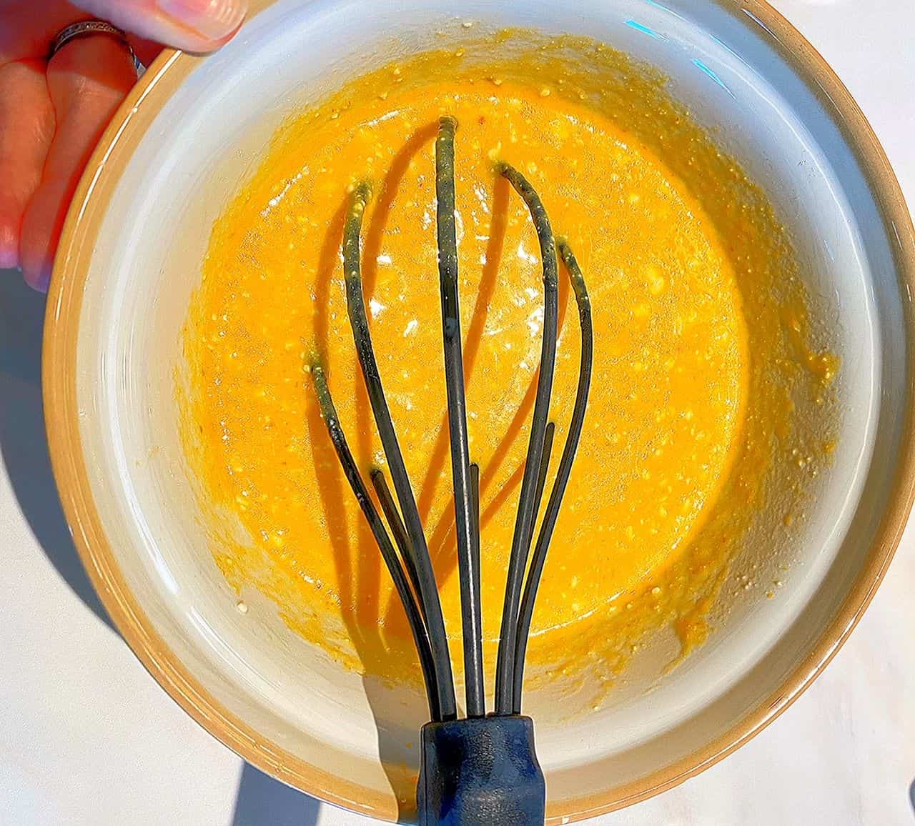 Large black whisk in light orange batter in tan-rimmed bowl