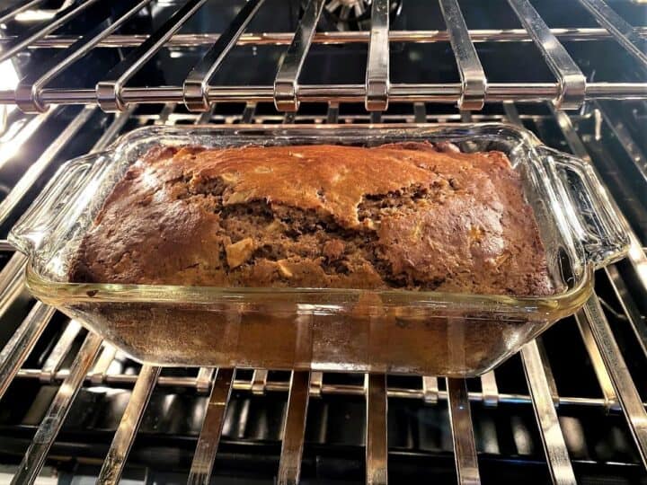 Golden apple pear with a crack on top baking in a clear glass loaf pan inside the oven.