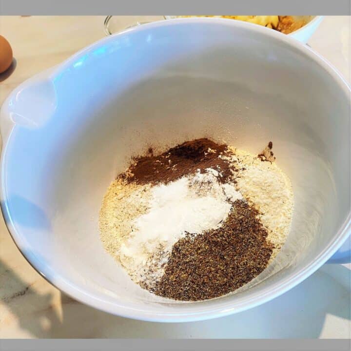 In a white, spouted bowl are dry ingredients--Flour, flax, spices, leaveners-- needed for apple pear bread.