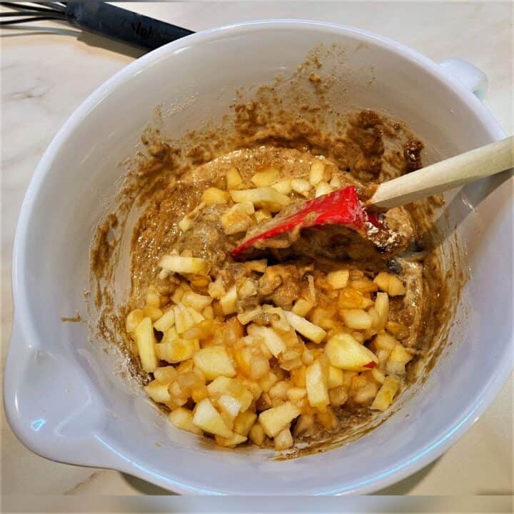 Chunks of apple and mushy pear being mixed with a red spatula into the light brown apple pear bread batter.