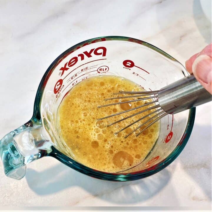Using a steel whisk to combine wet ingredients for apple pear bread into yellow-brown liquid in a glass pyrex measuring cup.