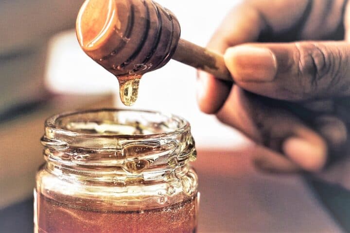 Hand with honey server dripping honey over a honey jar.