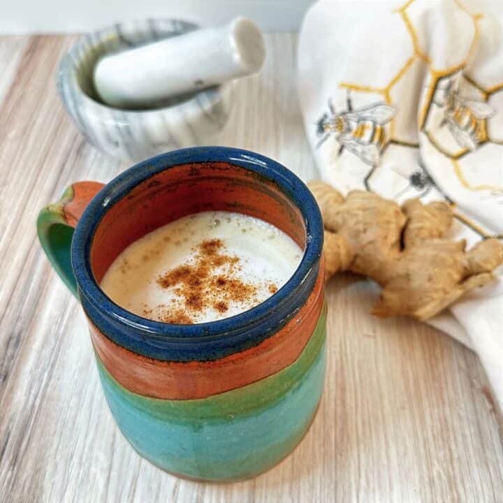 Colorful pottery mug with ginger milk tea and ginger root and marble mortar and pestle in the background.