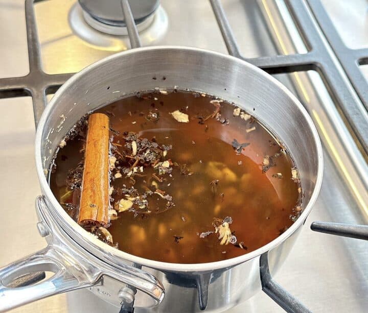 Black tea leaves and cinnamon stick steeping with ginger for tea in a saucepan.