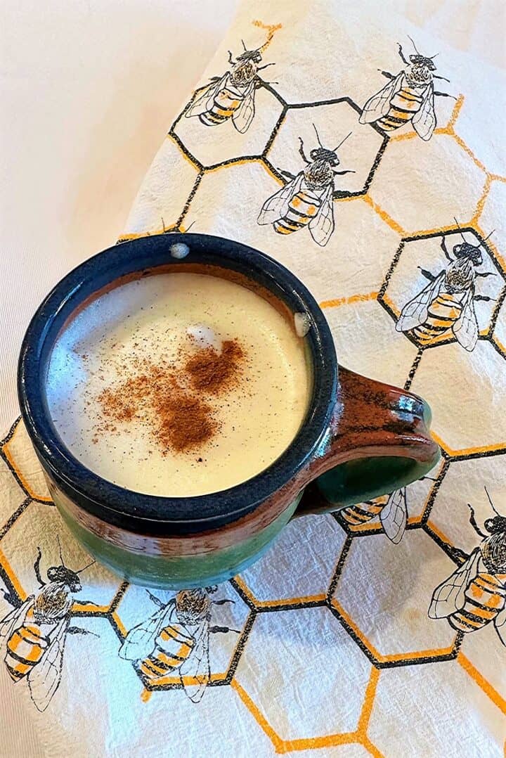 Colorful pottery mug of frothed ginger milk tea sprinkled with cinnamon against a honeycomb-bee kitchen towel.