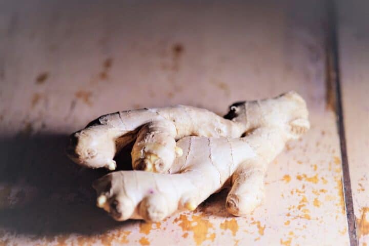 Unpeeled ginger root lying on a mauve peeling paint background.