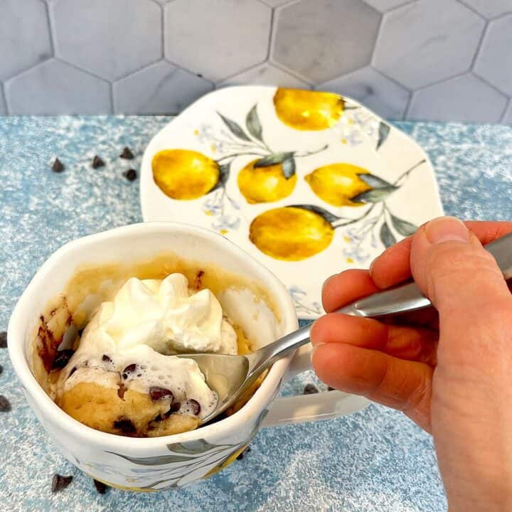 Spoonful of chocolate chip mug cake with whipped topping coming out of its cup.