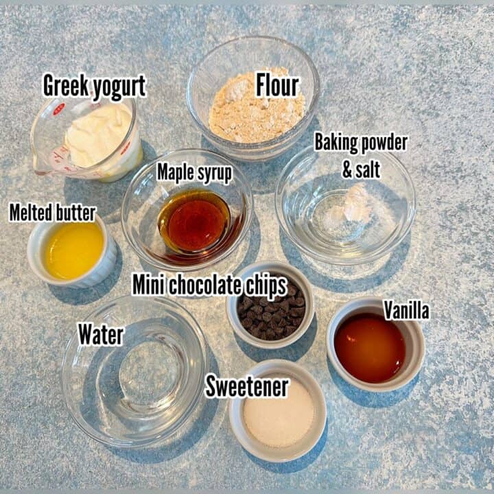 Ingredients for chocolate chip cake in a mug with labels on a mottled blue background.