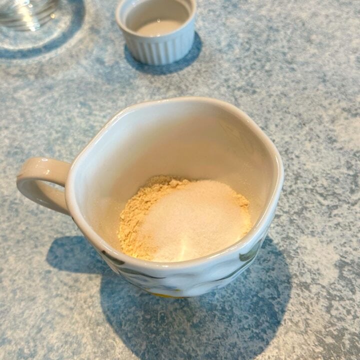 Tea cup with flour and other dry ingredients on mottled blue background.