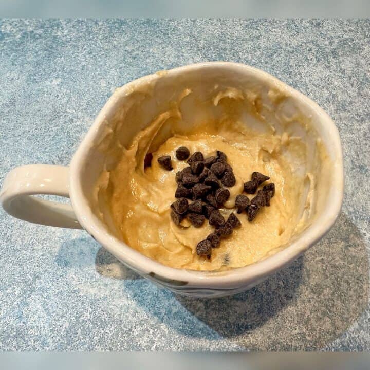 Mini chocolate chips in the center of the cake batter-filled tea cup on a bluish background.