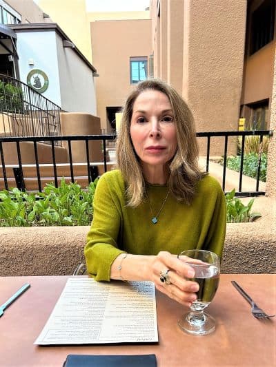 Jani Leuschel in a green sweater with a glass of water sitting at a patio table.