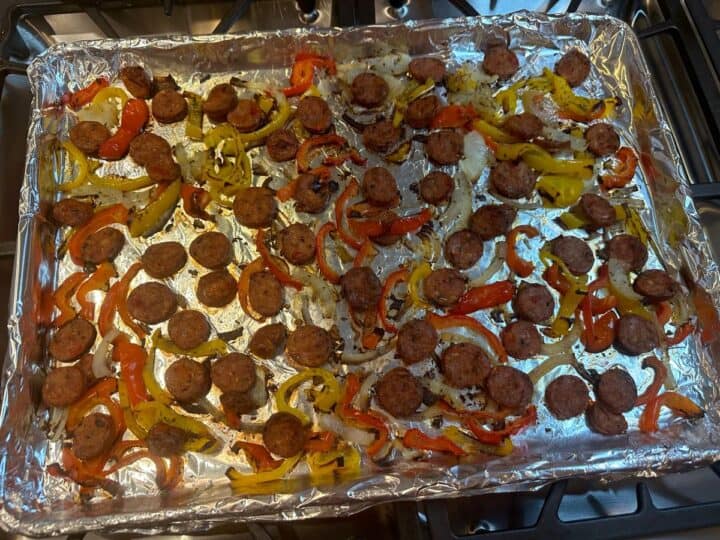 Sheet pan with cooked sausage rounds red and yellow peppers and onions slices that show golden and darker edges