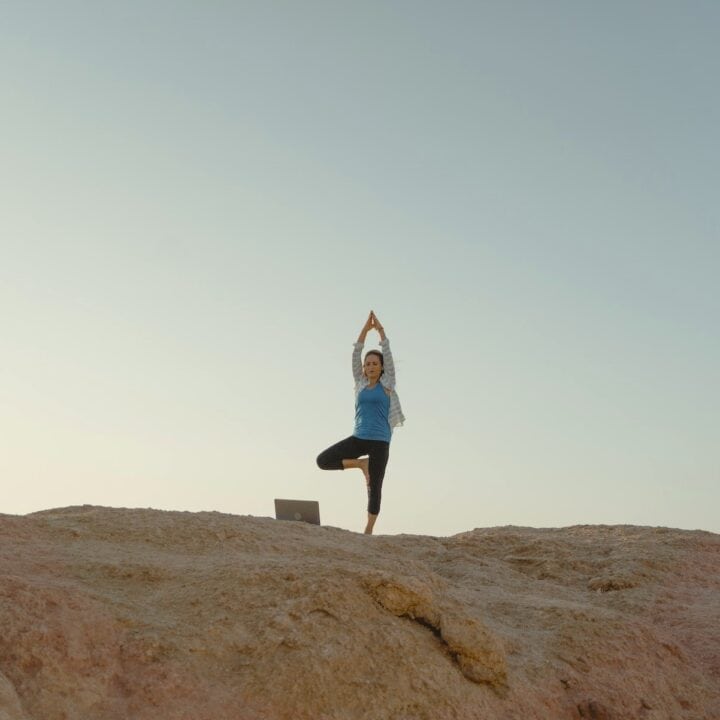 Woman standing on a cliff performing the tree pose on one leg