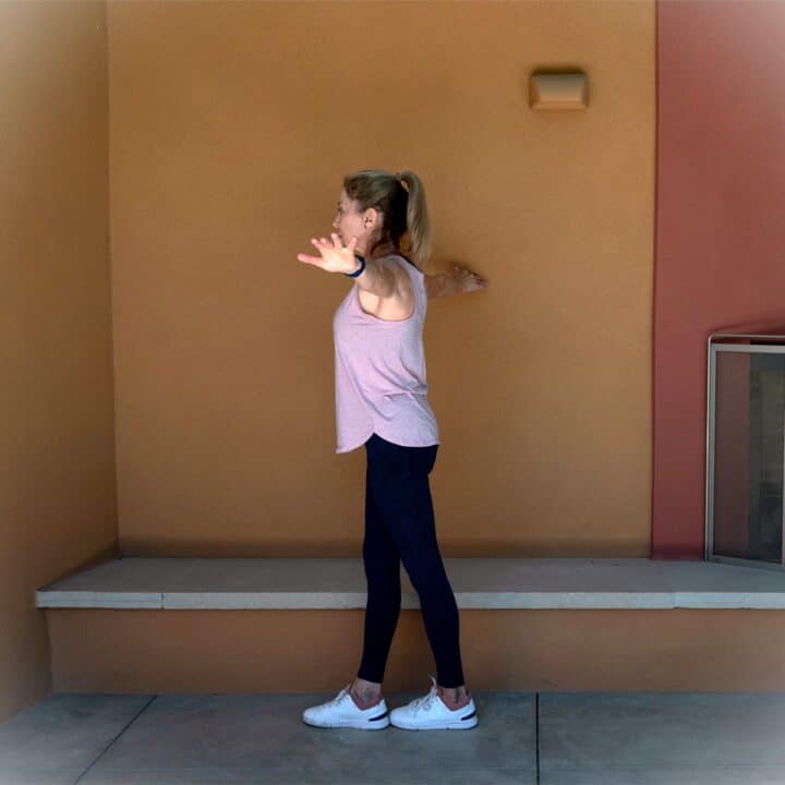 Woman in pink tank top and navy tights walking heel to toe and holding a golden stucco wall for balance.