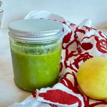 Green basil vinaigrette dressing in a round, clear jar with a whole yellow lemon on the side.