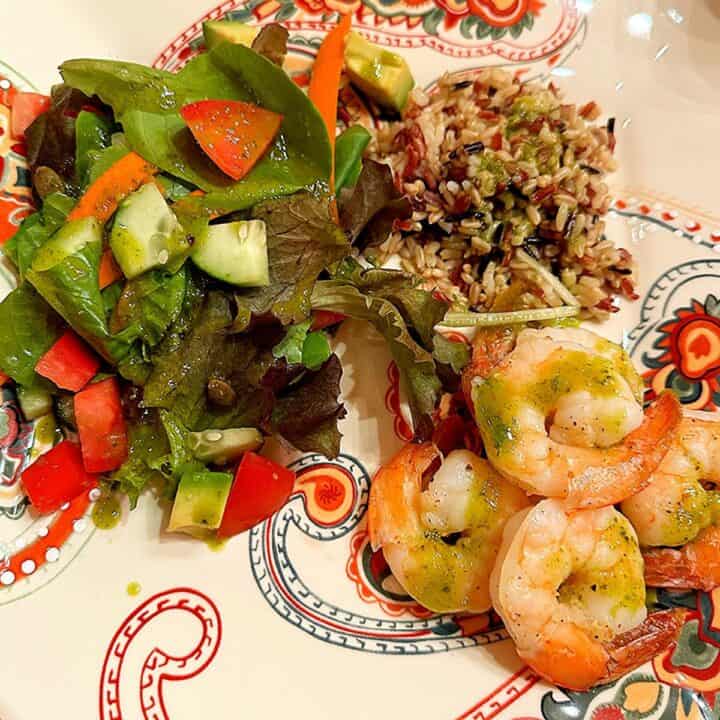 Shrimp, grains, and green salad sauced with green vinaigrette on a plate with paisley patterning.