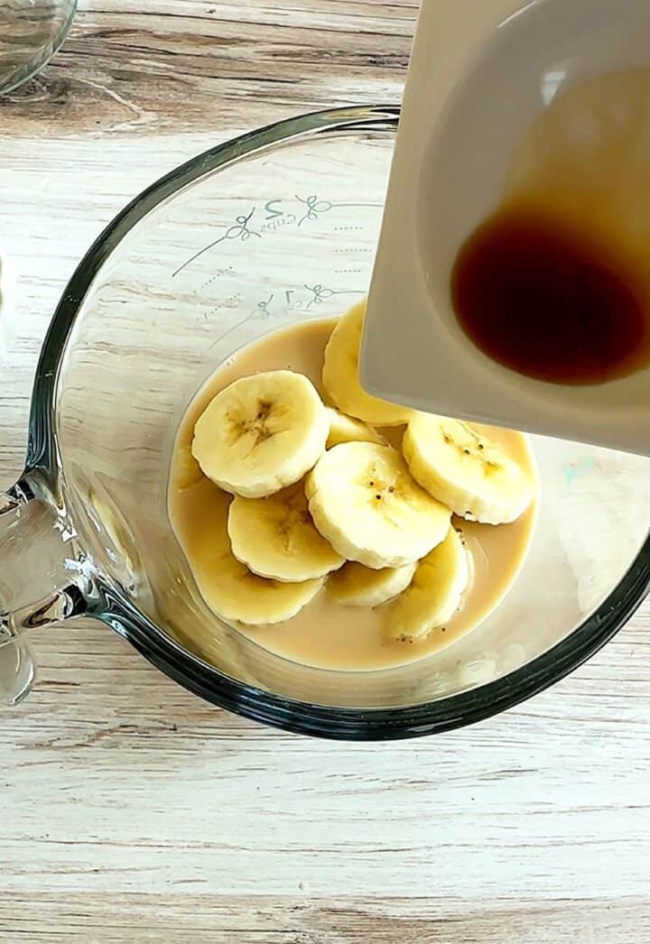 Adding brown flavorings to a  Measuring cup with oat milk, sliced bananas.