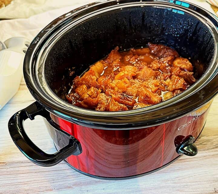 Brown, stewy, soft pears in a red crockpot with a black liner on a wooden background.