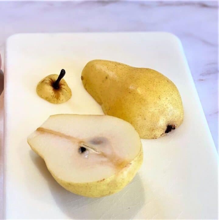 Yellow pear cut in half showing on white cutting board with marble background.