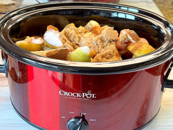 Pears fill a red crockpot and are topped with sugar and spices.