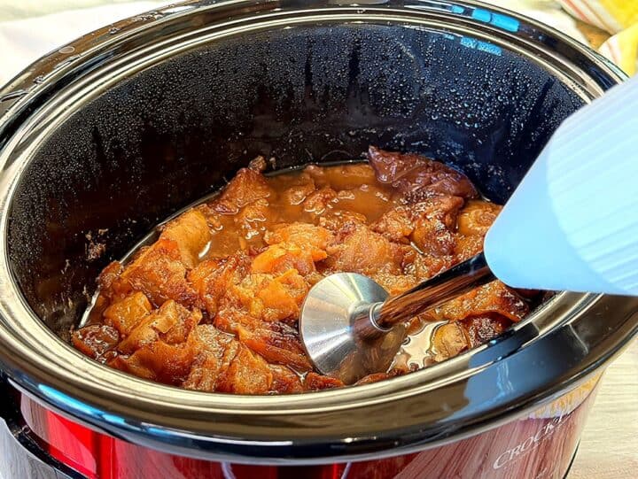 White stick blender with stainless steel shaft going into pear butter in the black liner of a red Crockpot.