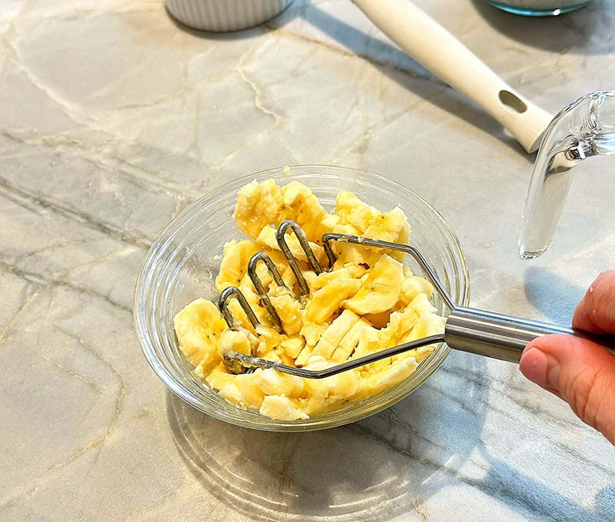 Mashing bananas in a small bowl with a small potato masher.