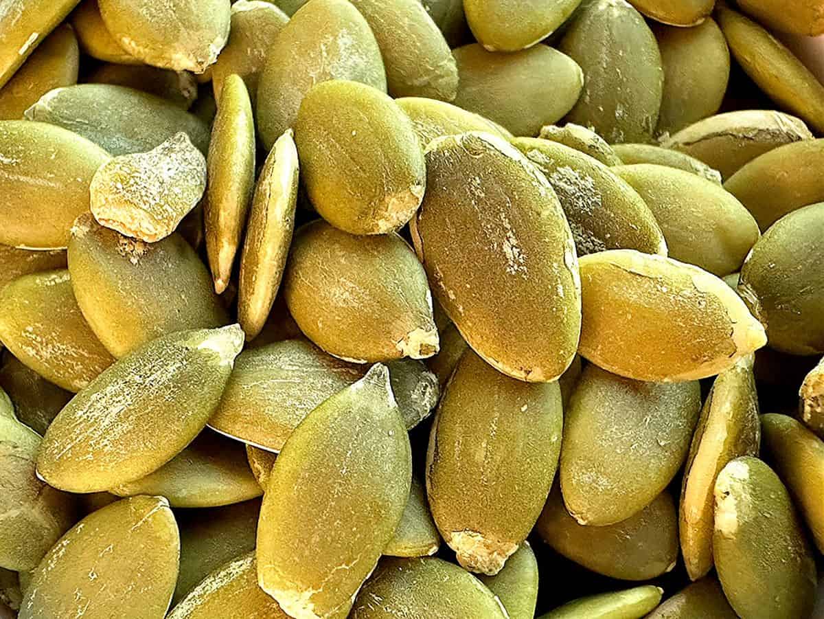 Green-gray pumpkin seeds fill the frame in a close-up.
