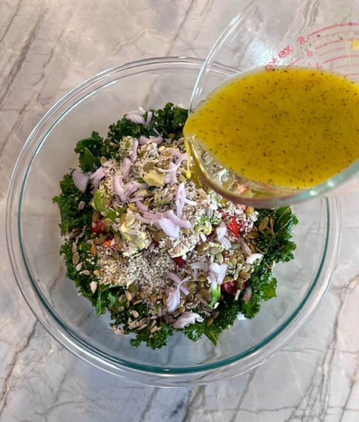 Pouring lemony dressing over a clear bowl of Kale White Bean Salad with avocado, shallots, and more!