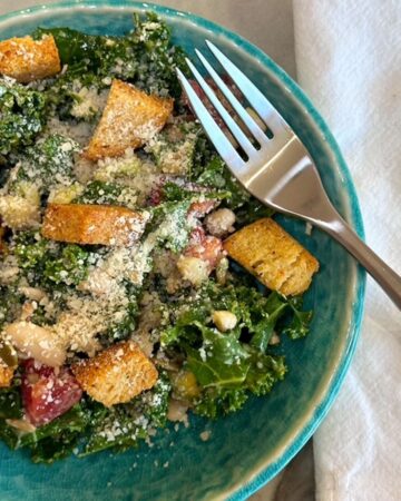 Dark green kale salad with croutons and a fork on a jewel-green plate.