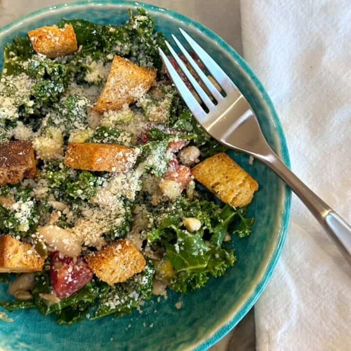 Dark green kale salad with croutons and a fork on a jewel-green plate.