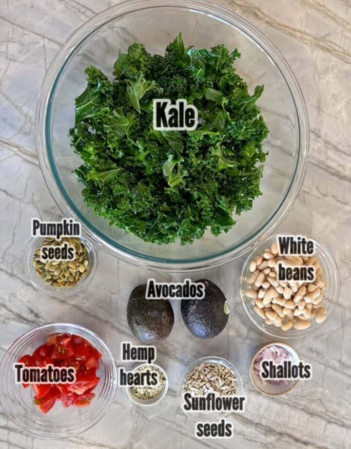 Chopped kale, white beans, red tomatoes, green avocados, and seeds for a kale white bean salad.