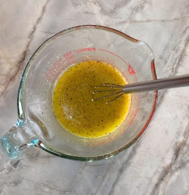 Clear Pyrex measuring cup with mustard-yellow dressing and small whisk.