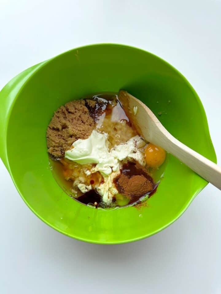 White yogurt, brown sugar, syrup, egg, and other liquid ingredients in a lime green mixing bowl.