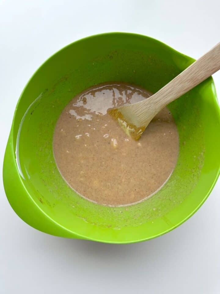Tan liquid with small pieces of banana in a lime green mixing bowl.