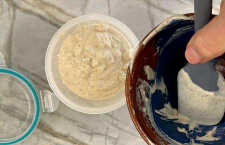 Opaque container full of creamy tahini sauce with scraped clean brown bowl in the foreground over it.
