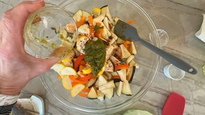 Clear bowl full of tender, chopped veggies wth a large dollop of green pesto on top.