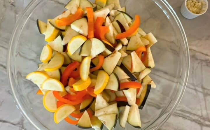 Large clear bowl full of colorful chopped veggies, including orange bell pepper and yellow squash. 