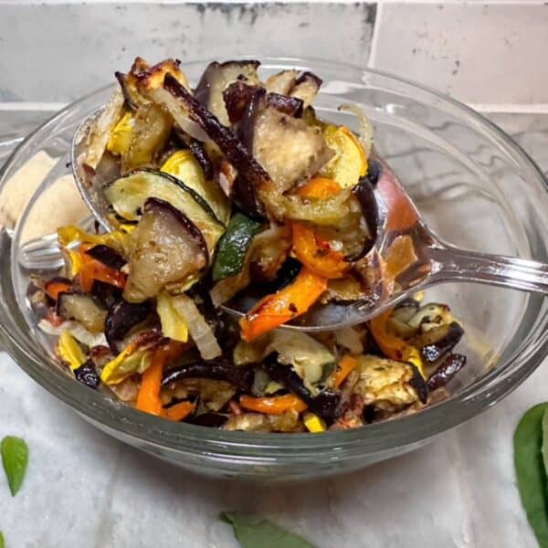 Close view of a clear bowl full of colorful pesto roasted vegetables with a large spoonful front and center.