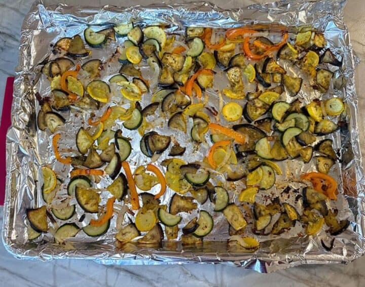 Foil-lined sheet pan full of brown-edged roasted tender veggies like eggplant, squash, and orange bell pepper.