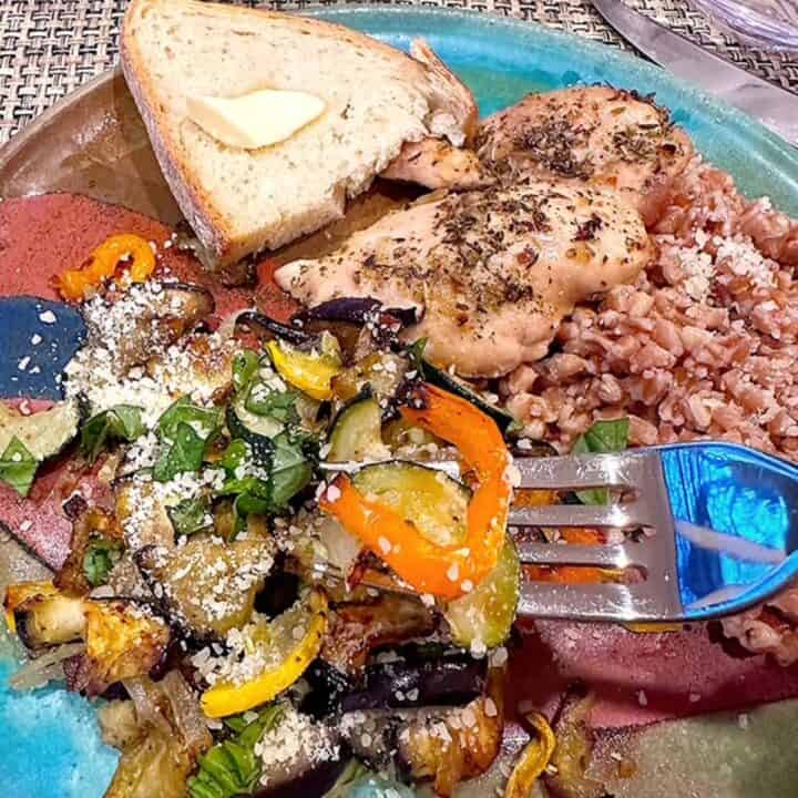 Colorful pottery plate holds a dinner of chicken with farro and colorful pesto roasted vegetables.