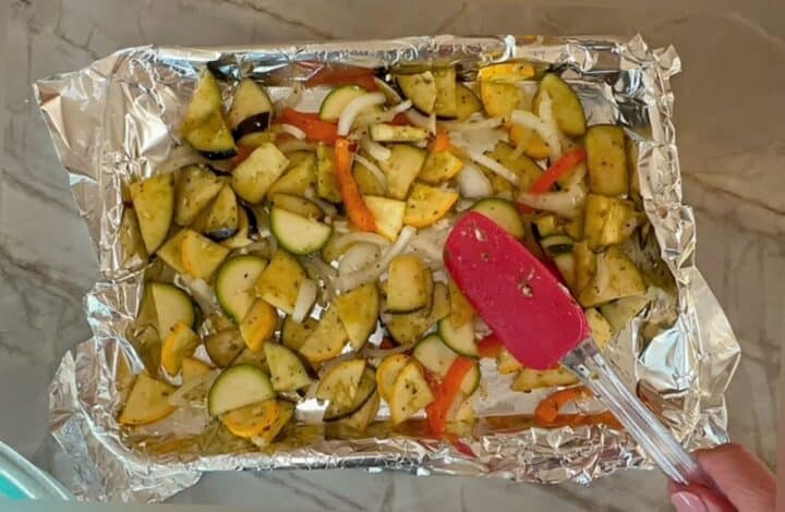 Foil-lined sheet pan full of raw vegetables tossed in pesto.