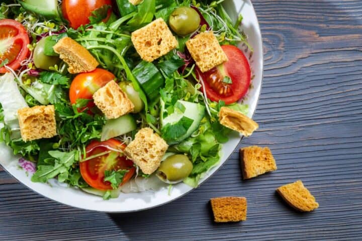 Green salad in white bowl with red halved cherry tomatoes and croutons.