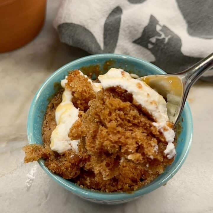 Metal spoon inserted in Green-blue ramekin with brown honey cake and white yogurt topping.