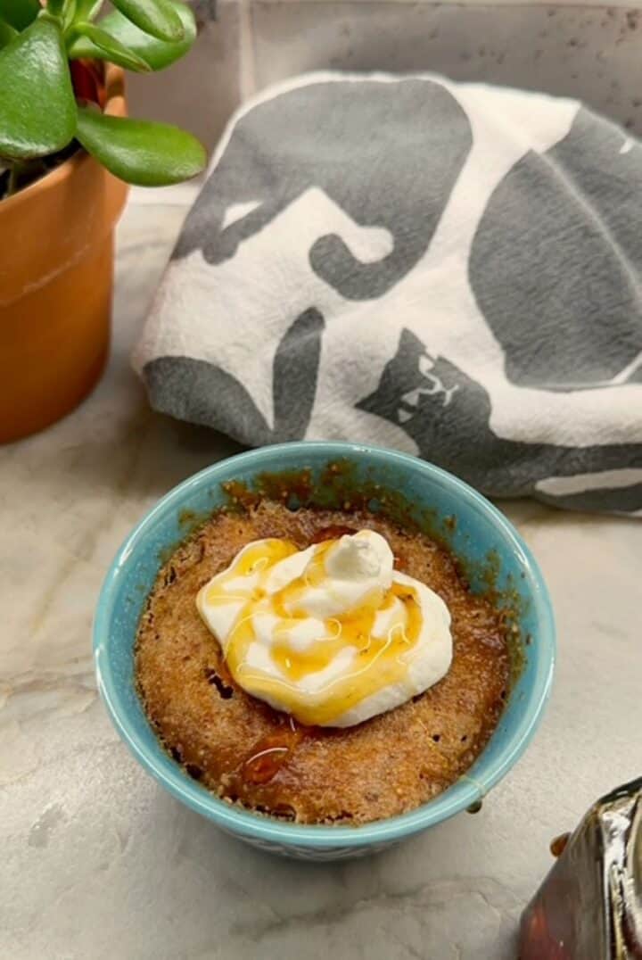 Brown Honey Almond Butter Cake in a blue-green ramekin with a white dollop of yogurt and amber honey drizzle.